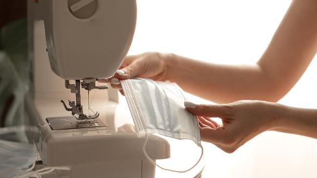 Woman hands using the sewing machine to sew the face medical mask during the coronavirus pandemia. Home made diy protective mask against virus. Woman hands using the sewing machine to sew the face medical mask during the coronavirus pandemia. Home made diy protective mask against virus.